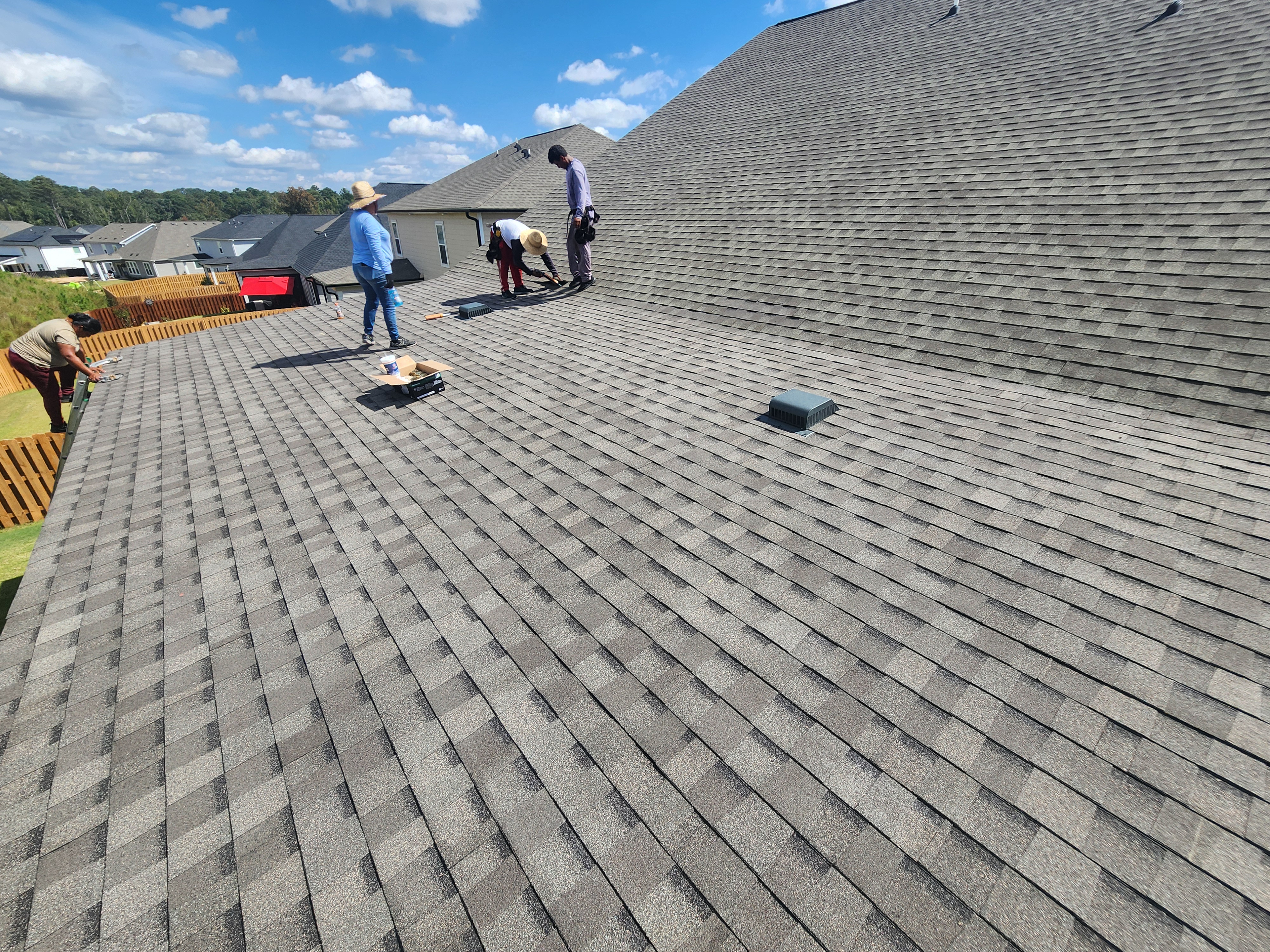 Crew laying shingles on a large roof